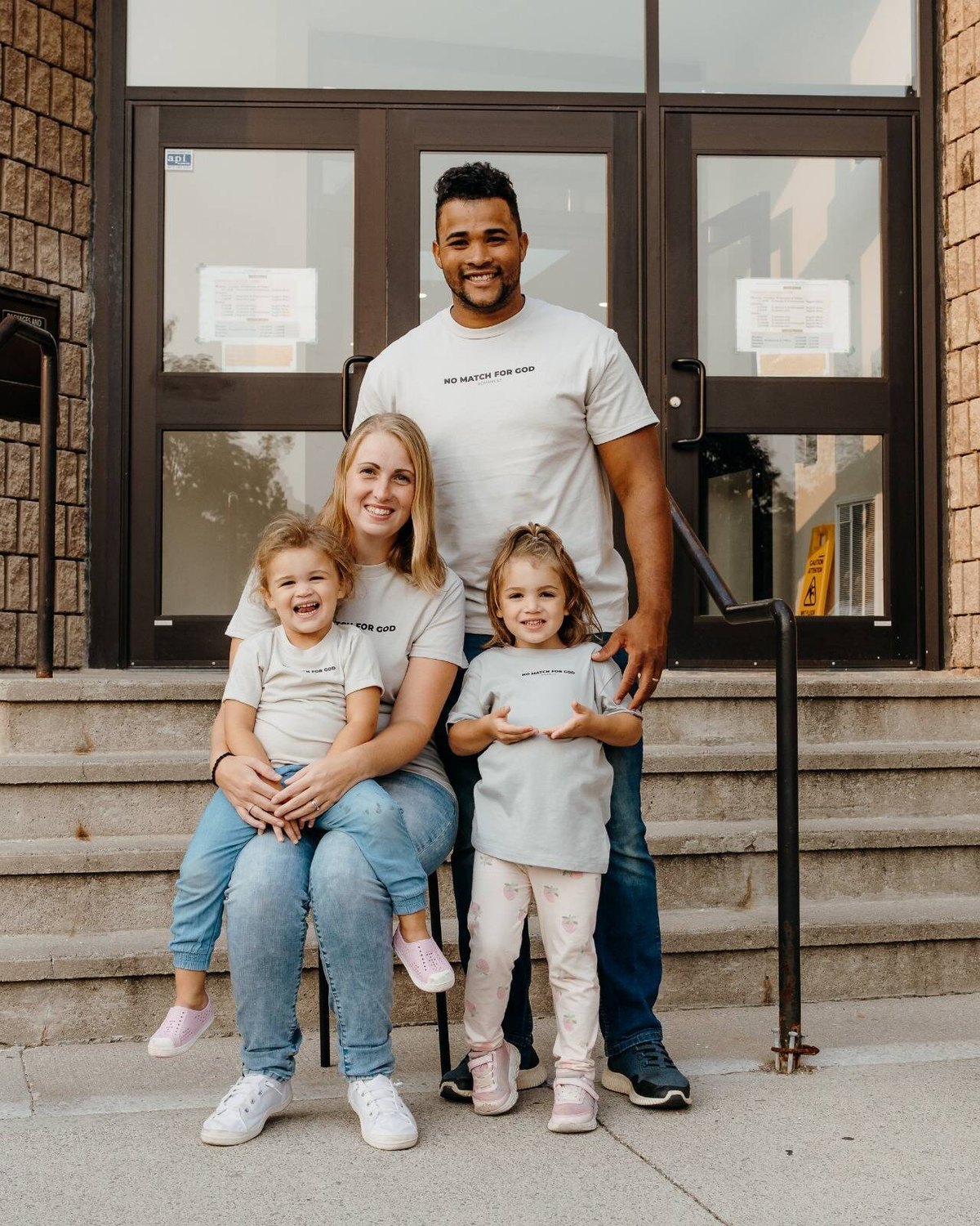 Isai and Kaitlin Balbuena with their two young daughters, standing on the steps outside the clinic.