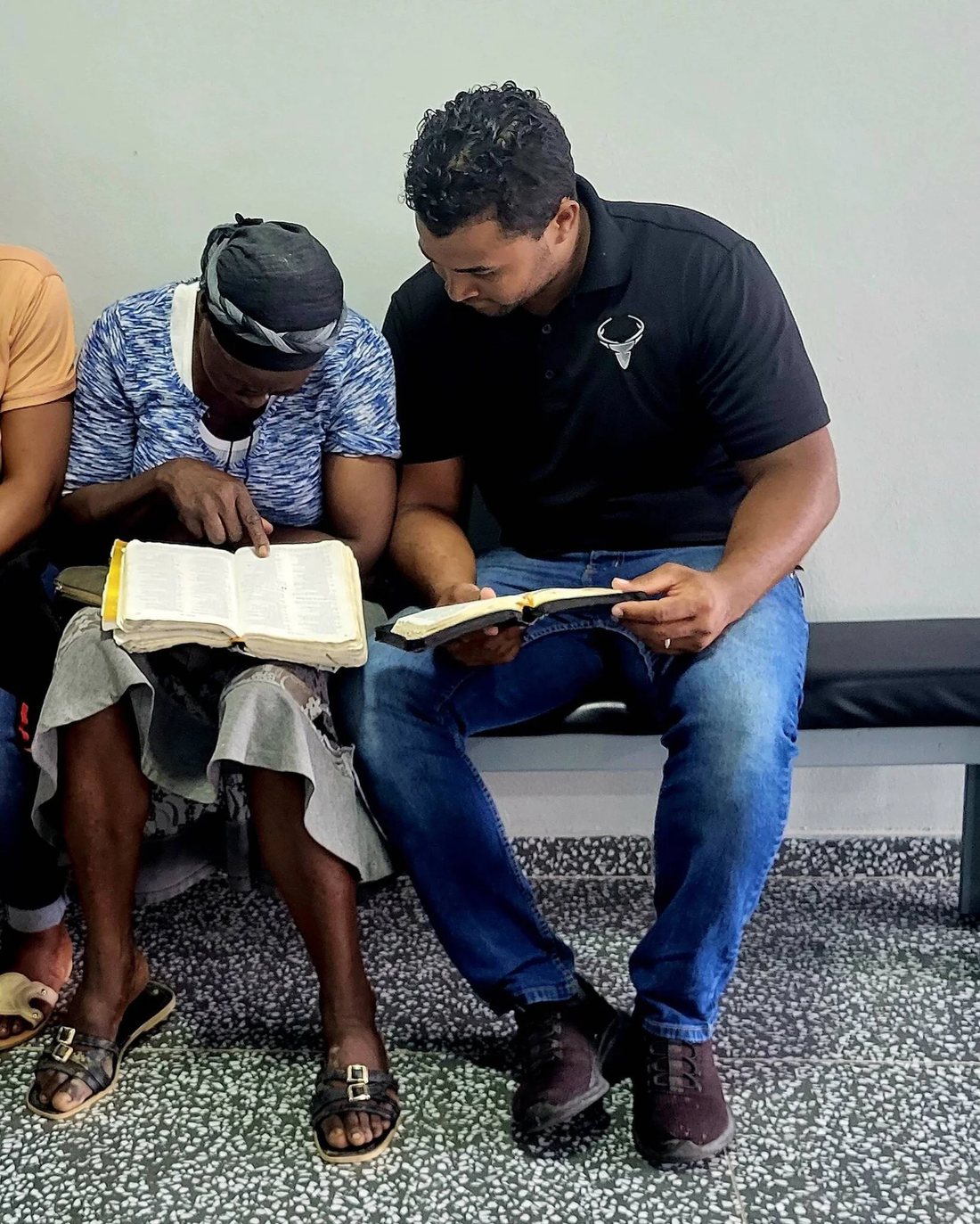 Isai sitting beside a patient in the clinic waiting area, reading the Bible together.
