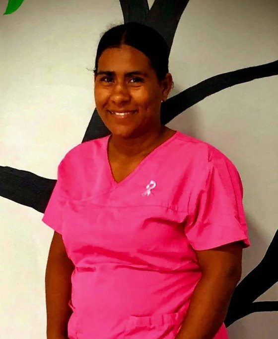 Nurse Adriana, wearing pink scrubs, in front of the clinic's tree mural.