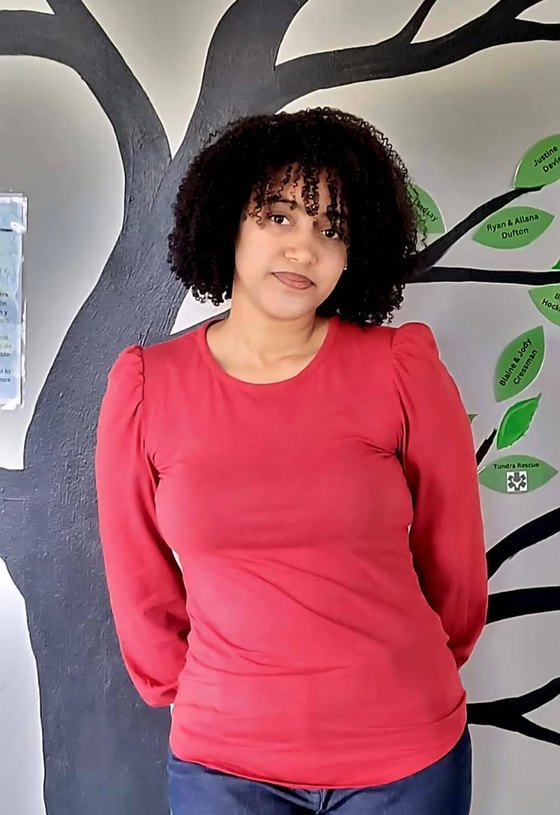 Pharmacy assistant Estrella, wearing a red top, in front of the clinic's tree mural.