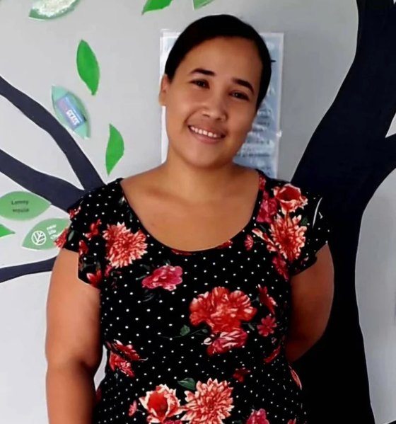 Secretary Keila, wearing a floral dress, in front of the clinic's tree mural.