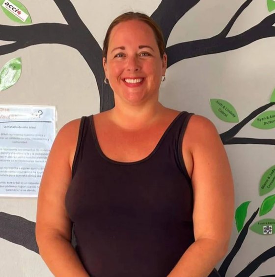 Volunteer Michelle, wearing a black top, in front of the clinic's tree mural.